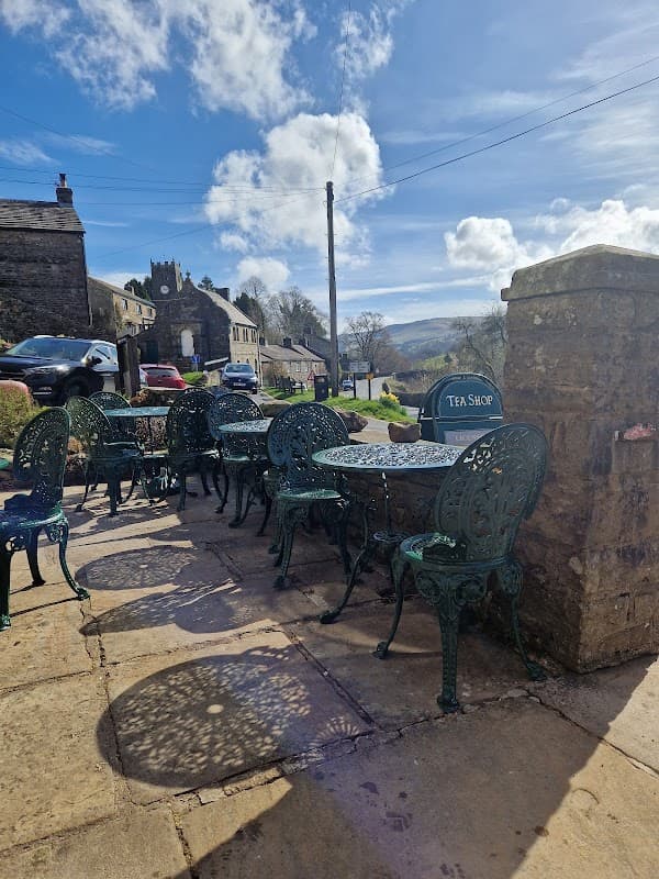 Quaint outdoor seating with green chairs and tables at Muker Village Store & Teashop, set against a scenic backdrop.