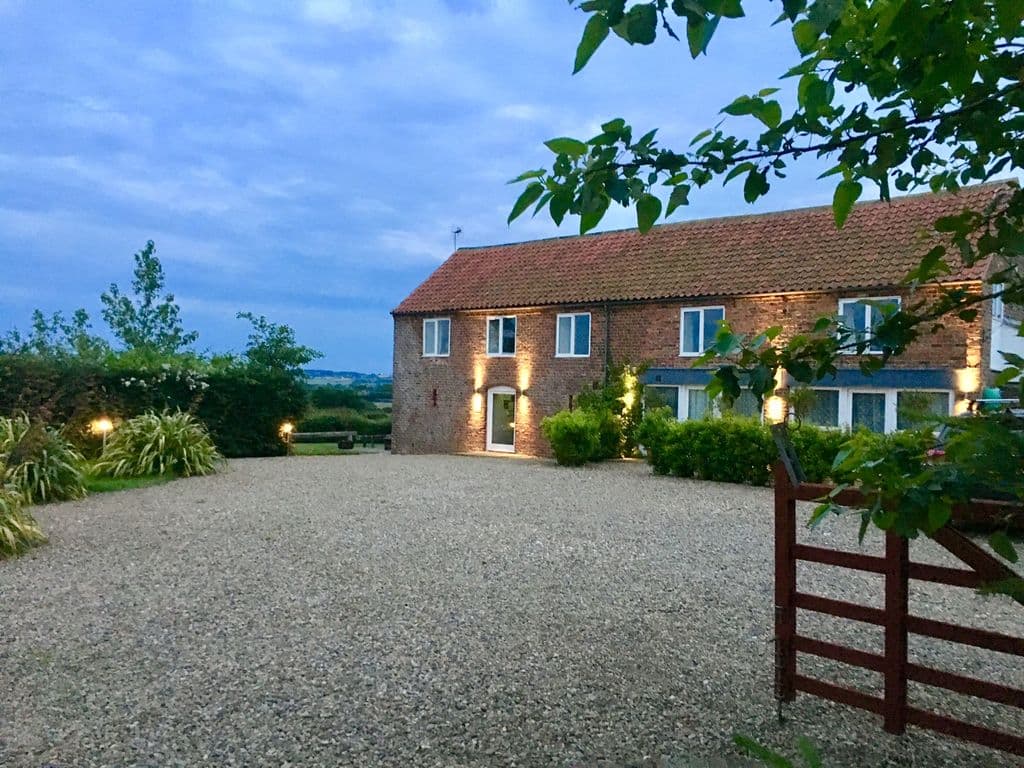 Charming brick holiday cottage with a gravel driveway, surrounded by greenery and evening sky in Muston, North Yorkshire.