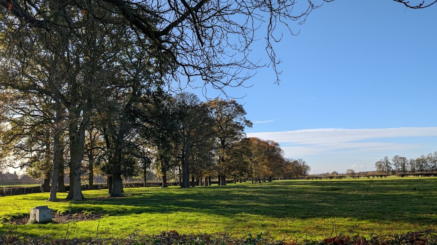 Lush green fields with tall trees under a clear blue sky at Myton Hall, Myton-on-Swale, Yorkshire.