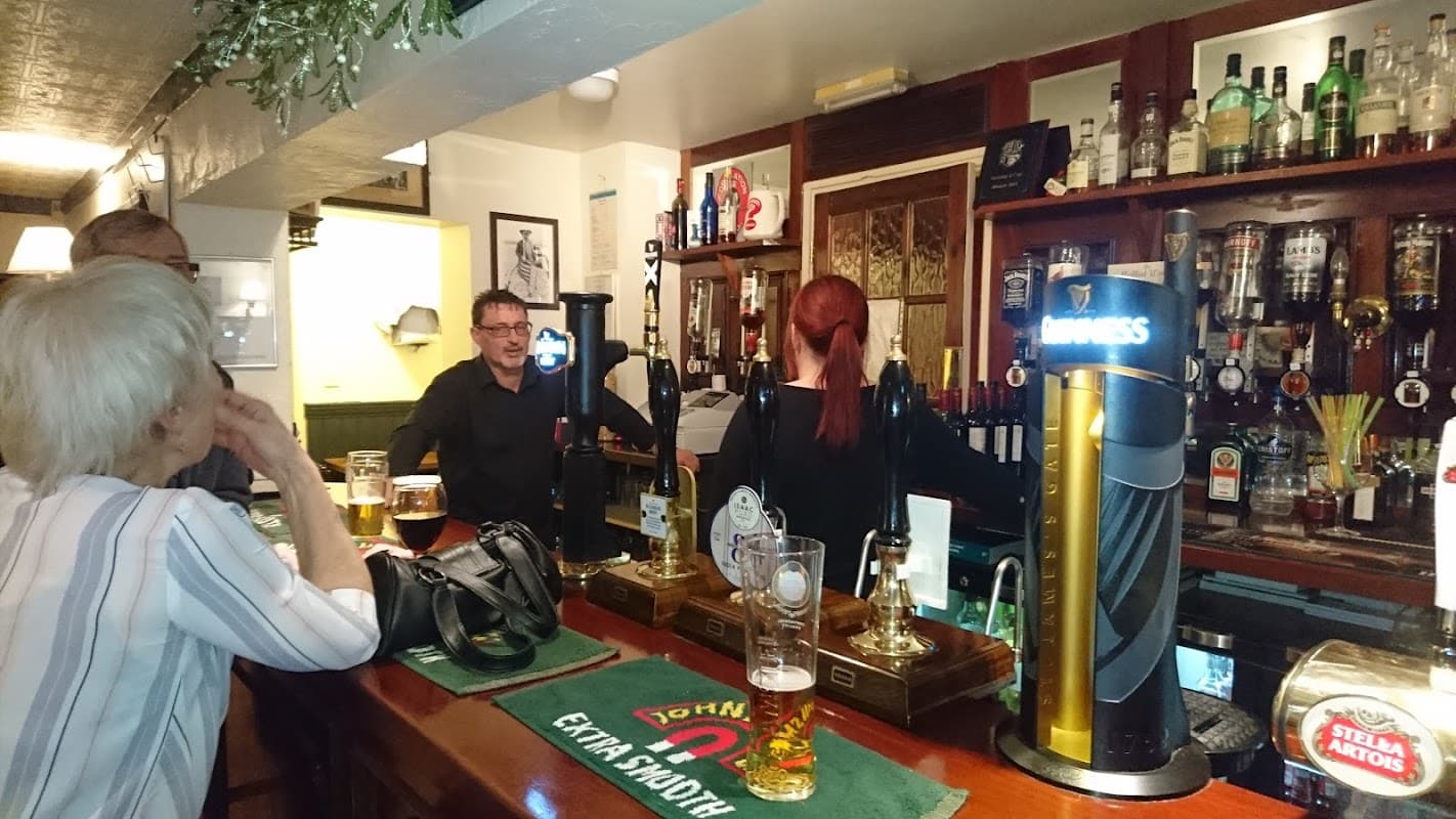 A bar scene at The Cross Keys, featuring patrons, beer taps, and shelves lined with various liquor bottles.
