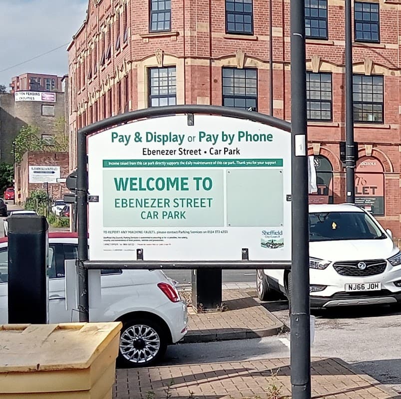 Sign for Ebenezer Street Car Park with parking instructions, surrounded by buildings and parked cars.