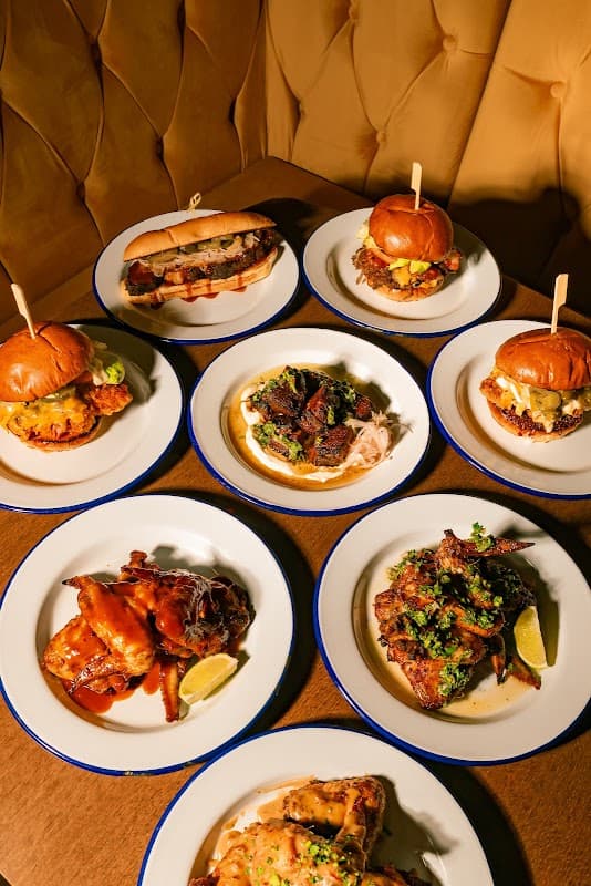 A spread of various dishes including poutine, burgers, and chicken wings on white plates against a brown table.