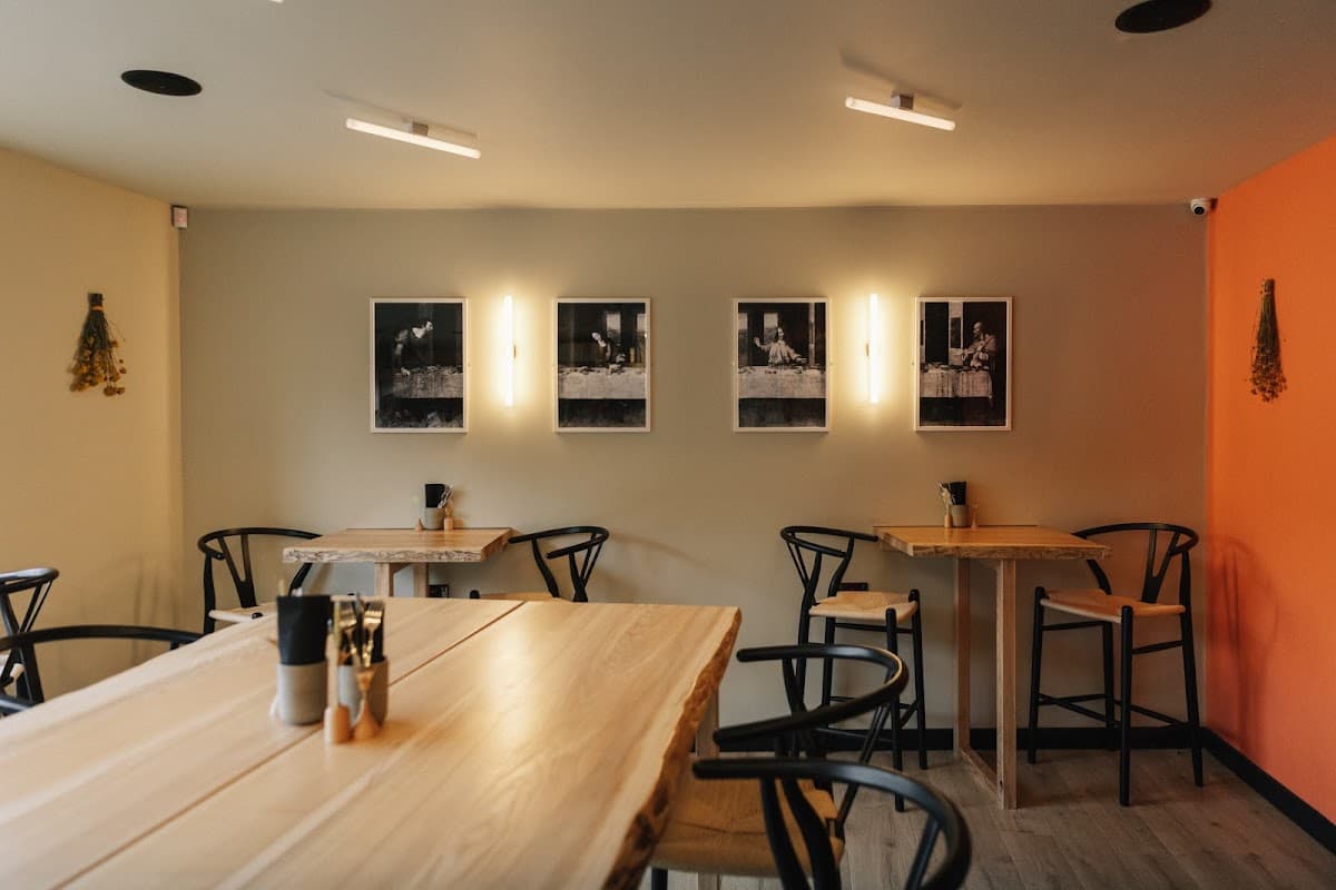 Stylish cafΓ© interior with wooden tables, black chairs, and framed black-and-white photos on the wall.