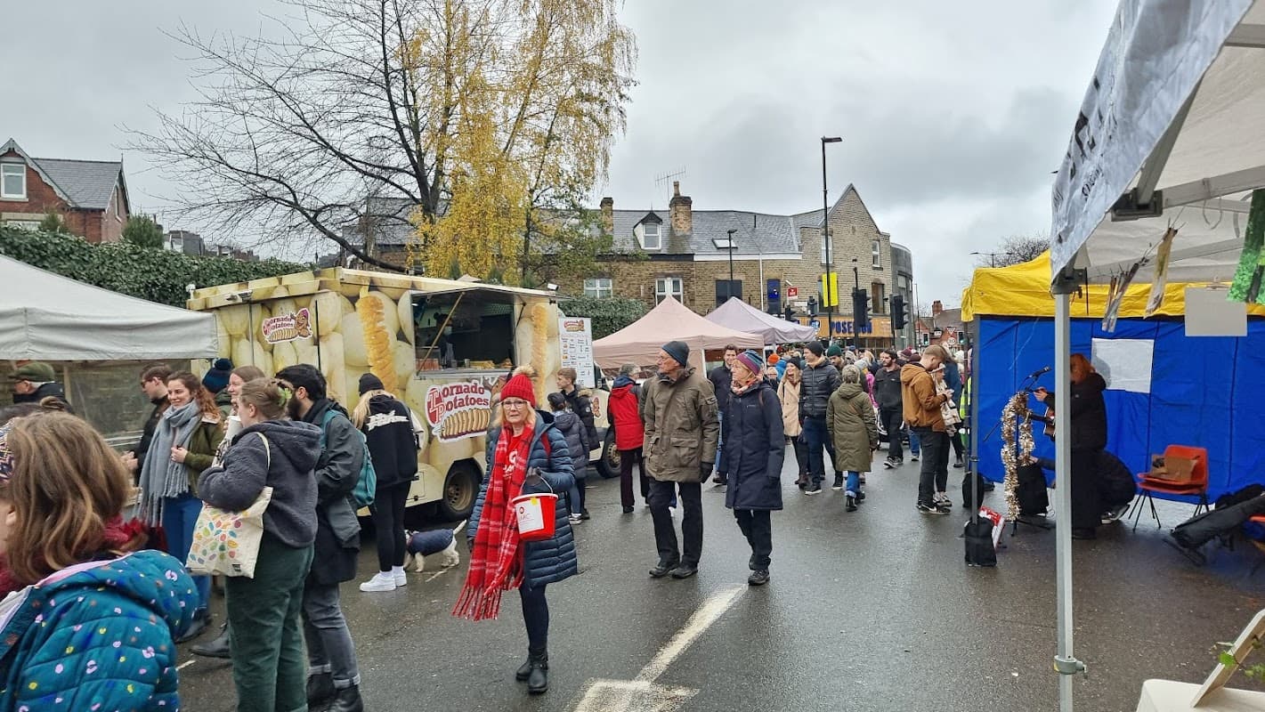 Busy market scene with stalls, people browsing, and food trucks under a cloudy sky in Nether Edge, Sheffield.