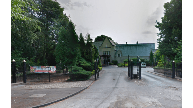 Entrance to a car park with gates, surrounded by trees and a banner, leading to a large building in Nether Edge, Yorkshire.