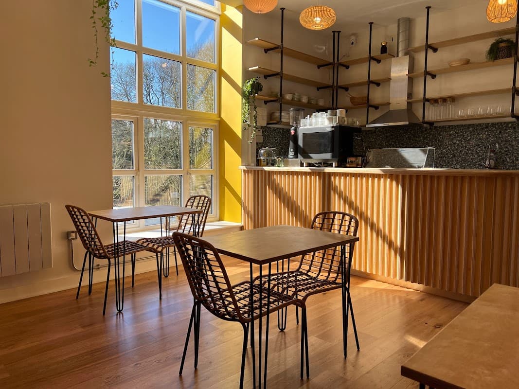 Bright café interior with wooden tables, woven chairs, and a coffee counter against a sunny window backdrop.