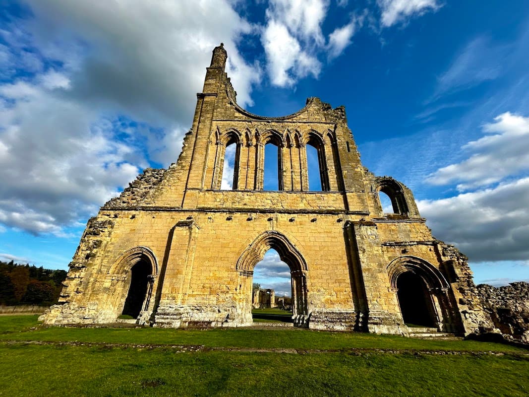 Ruins of Byland Abbey with tall stone walls, arched windows, and a dramatic sky in Newburgh, North Yorkshire.