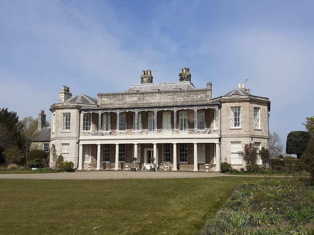 Historic building with a grand facade, large windows, and a balcony, set in landscaped grounds under a blue sky.