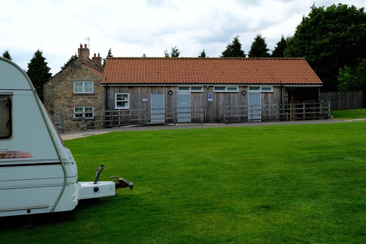 Wooden building with three doors, grassy area, and a caravan in the foreground, set in a rural Yorkshire landscape.