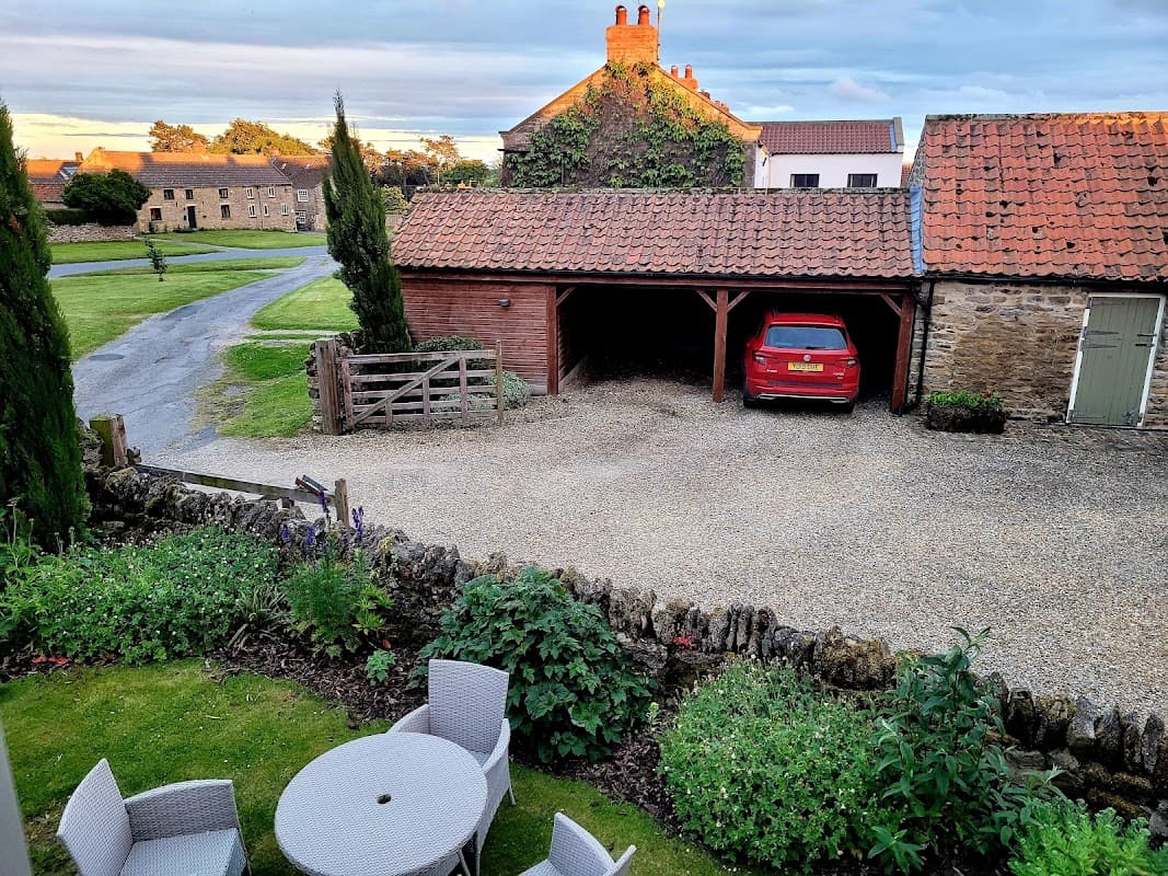 Pond Farm Bed & Breakfast features a gravel driveway, a red car, and outdoor seating among lush greenery.