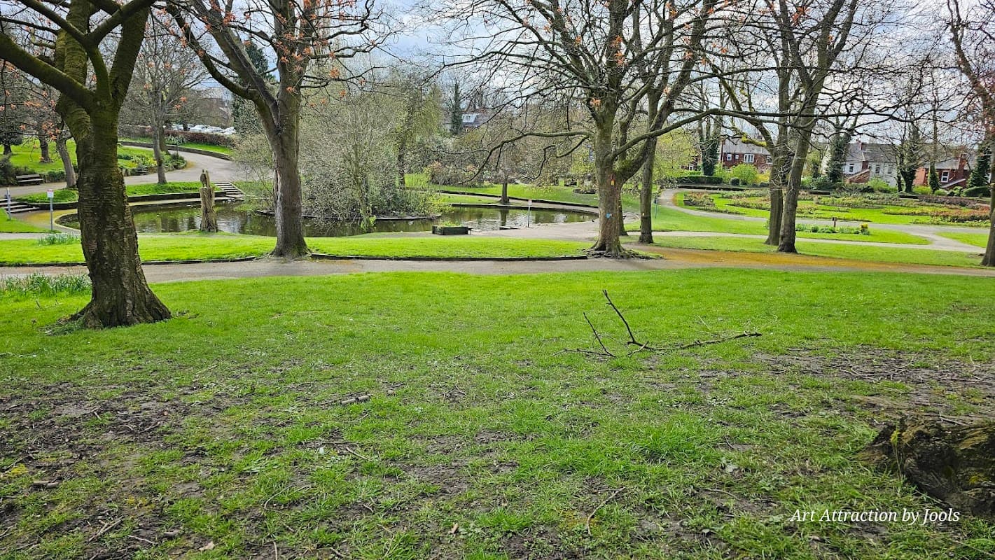 Lush green grass and trees surround a serene pond with winding paths in Haw Hill Park, Normanton, Yorkshire.