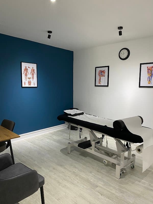 Bright therapy room with a treatment table, anatomical posters, a clock, and modern furnishings.