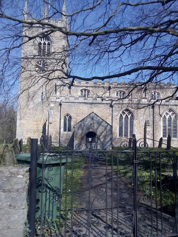 Stone church with a tall clock tower, surrounded by trees and a wrought iron gate, under a clear blue sky.