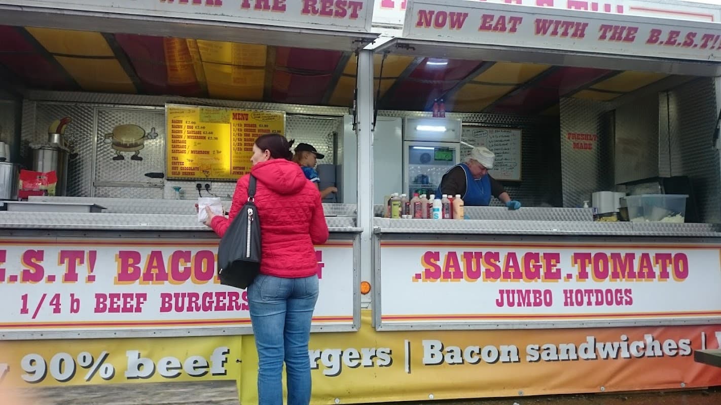 Food stall at North Cave Market with staff serving burgers and hot dogs; customer ordering with red jacket.