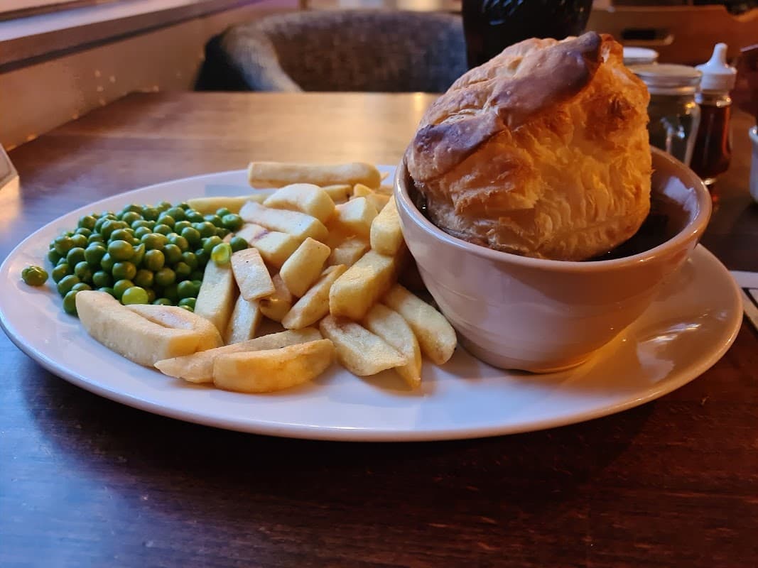A plate with chips, green peas, and a large pie on a wooden table.