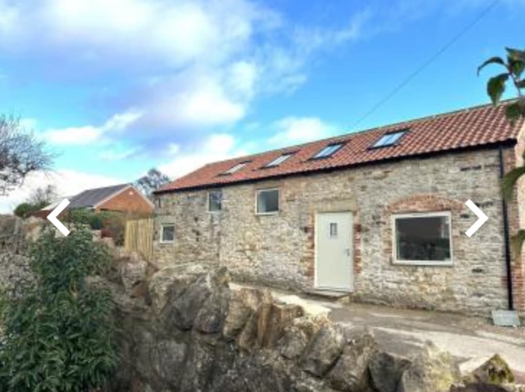 Stone building with a red-tiled roof, windows, and a door, set against a blue sky in North Cowton, Yorkshire.
