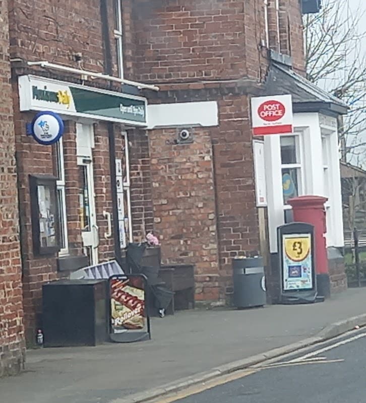Morrisons Daily grocers with a Post Office sign, red post box, and a display of snacks outside on a brick building.