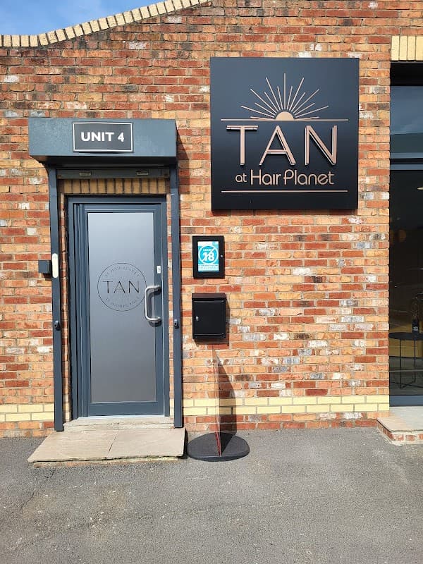 Entrance to TAN at Hair Planet, featuring a stylish door, brick wall, and sign with sunburst design.