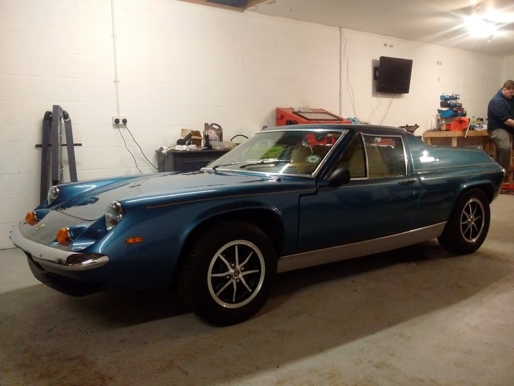 Classic blue sports car in a garage, with tools and equipment visible in the background.