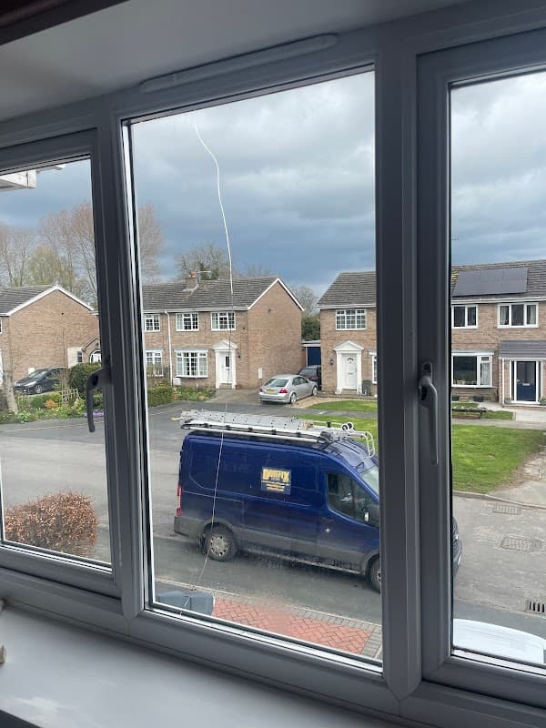 View through a window showing a blue van parked in front of houses under a cloudy sky in North Frodingham.