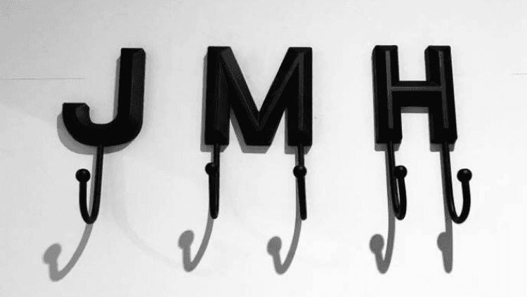 Black metal hooks shaped like the letters J, M, and H, casting shadows on a white wall.