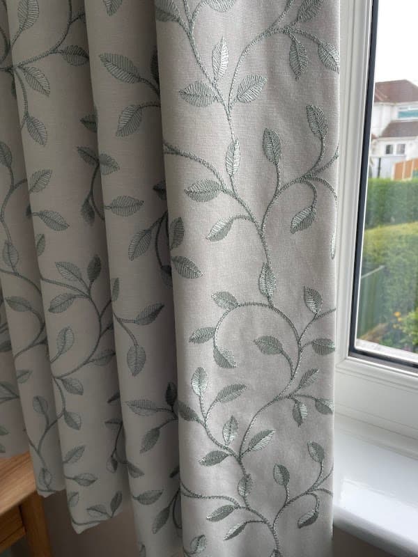 Light-colored curtains with a delicate leaf pattern, hanging by a window with greenery visible outside.