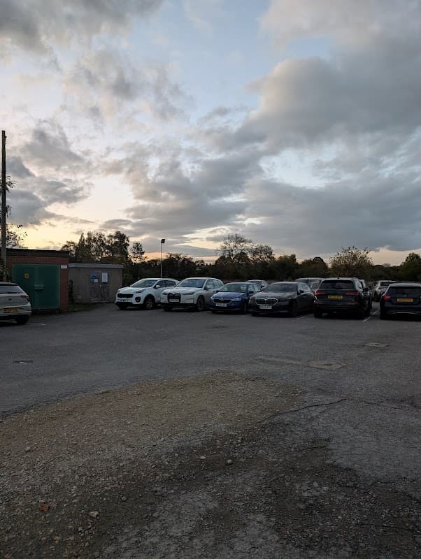 Car park with various parked cars, cloudy sky, and a green utility shed in the background.