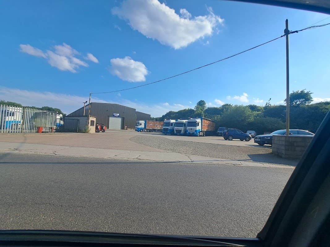 Cullingworth Commercials Ltd yard with trucks, cars, and a large industrial building under a blue sky.