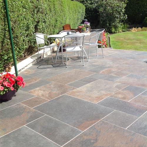 Paved outdoor area with a table and chairs, surrounded by lush greenery and colorful flower pots.