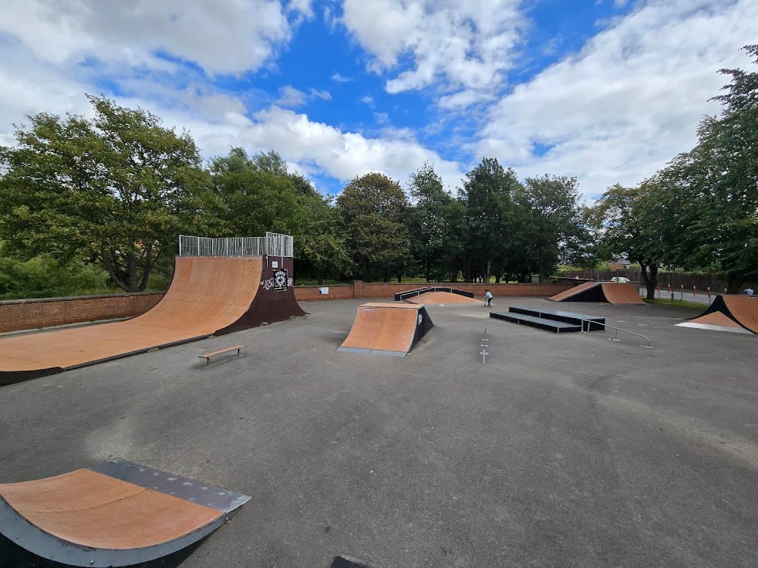 Skatepark featuring a vert ramp, various ramps, and rails surrounded by trees and cloudy sky in Norton, Yorkshire.