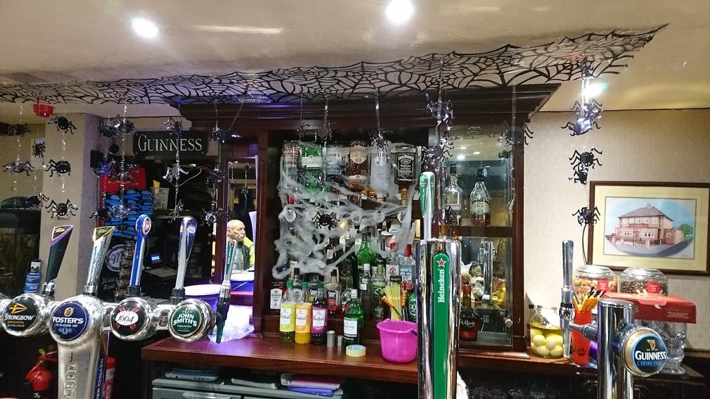 Bar counter with various drink taps, bottles, and Halloween decorations including cobwebs and plastic spiders.