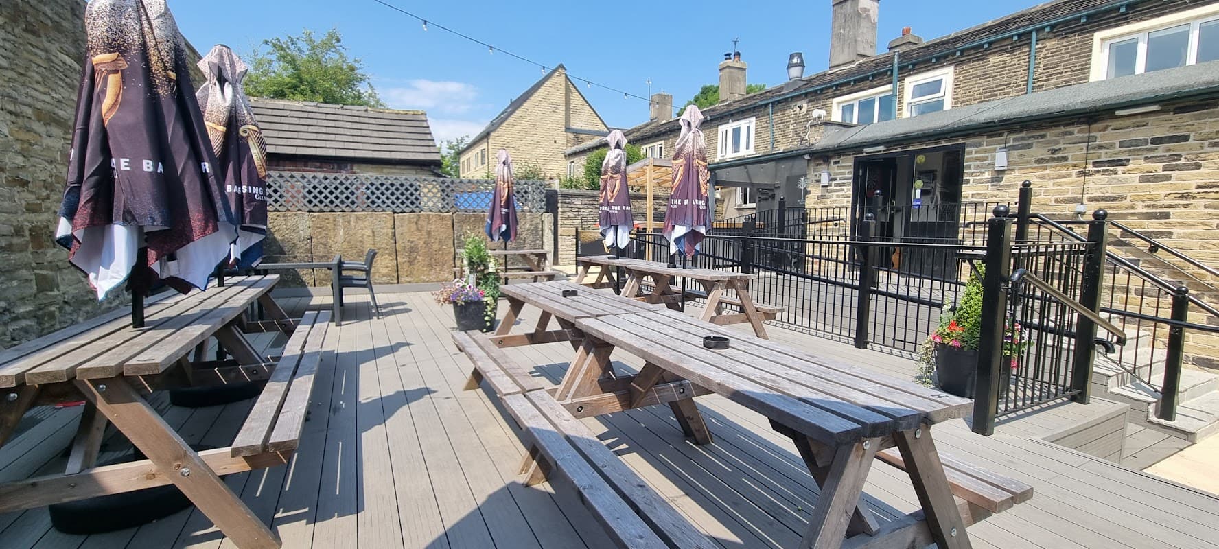 Outdoor seating area with wooden picnic tables, umbrellas, and planters at Pear Tree Bar in Norwood Green, Yorkshire.