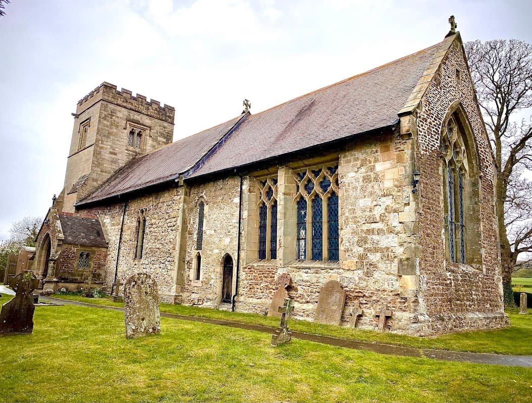 Historic stone church with a tall tower, arched windows, and a grassy cemetery in Nunburnholme, Yorkshire.