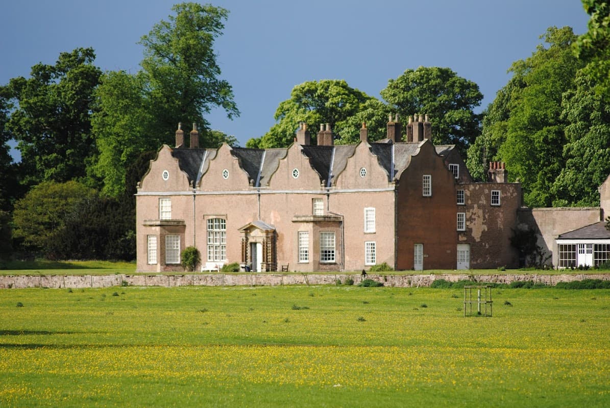Historic stone house with large windows, surrounded by lush greenery and a vibrant yellow flower field.