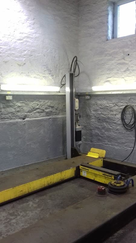Workshop interior with a yellow platform lift, stone walls, and overhead lighting.