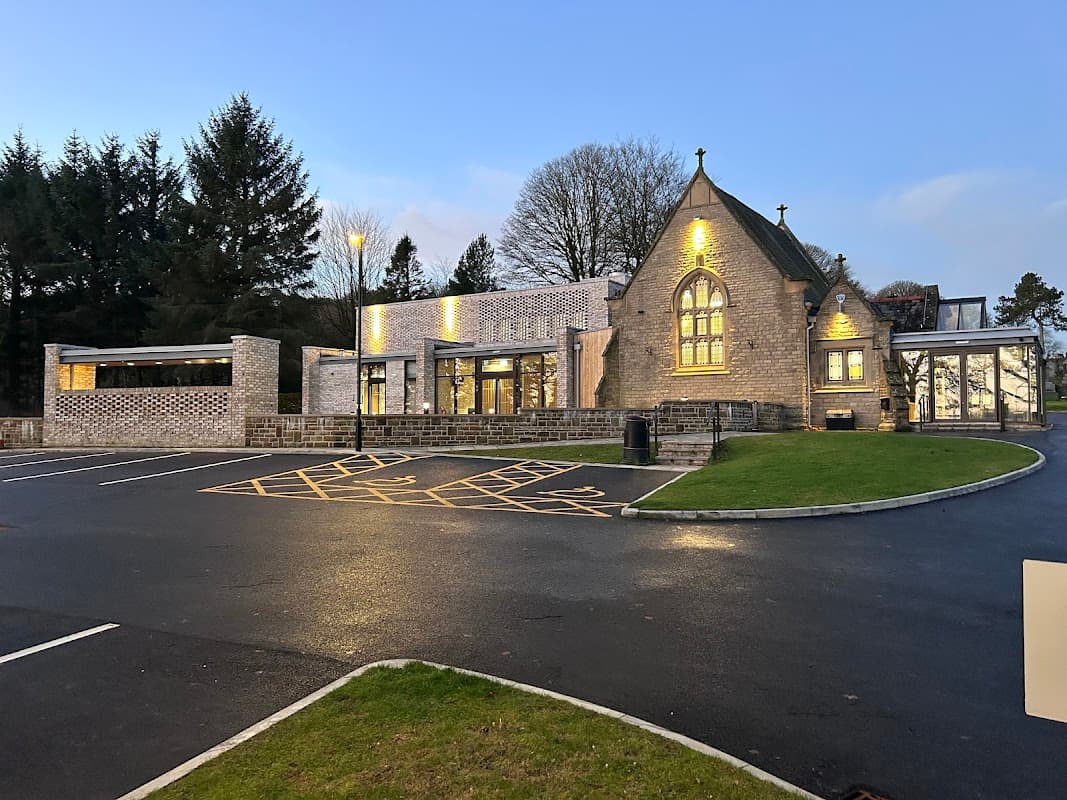 Modern stone building with large windows, surrounded by trees and a paved car park in Oakworth Cemetery, Yorkshire.
