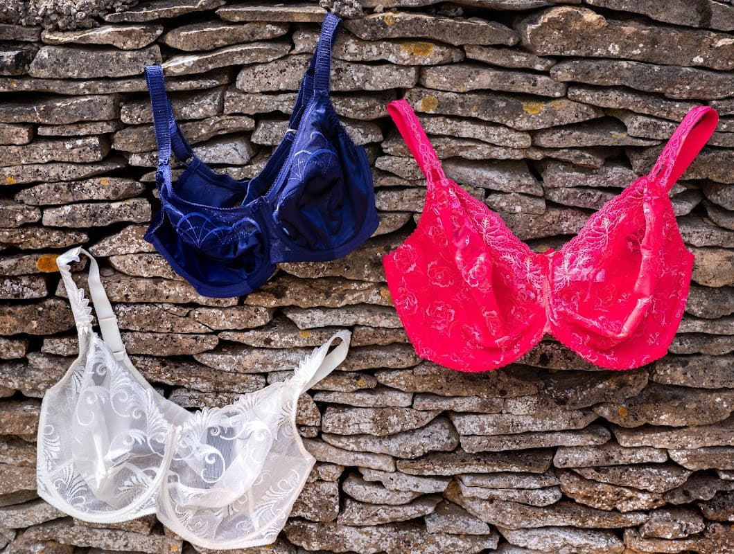 Three bras in navy, white, and pink displayed against a rustic stone wall in Old Byland, Yorkshire.