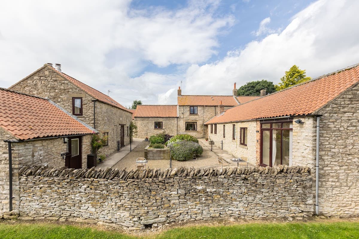 Charming stone cottages with red roofs and a landscaped courtyard, surrounded by a dry stone wall in Old Byland.