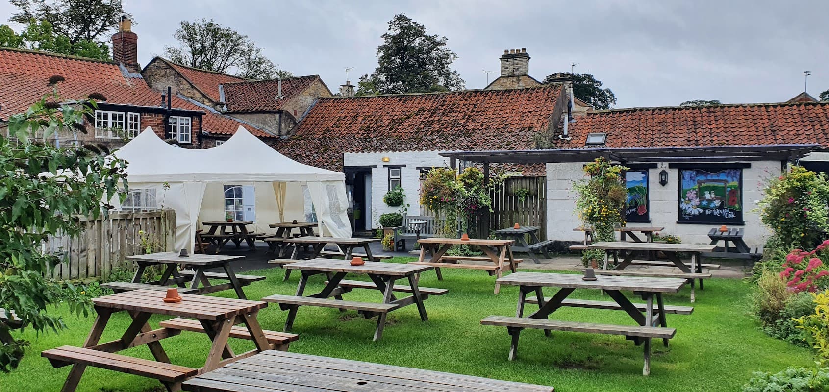 Outdoor seating area with wooden picnic tables, a white marquee, and a charming pub building in Old Malton, Yorkshire.