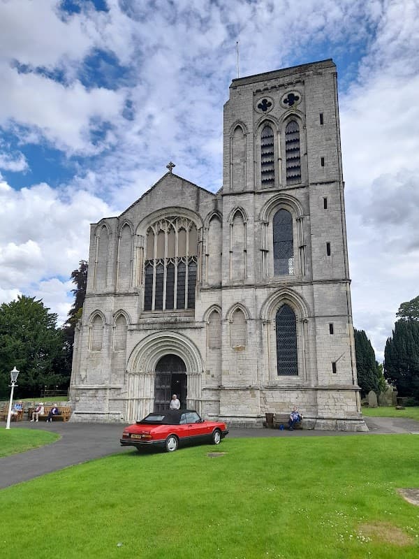 St Mary's Priory Church features a tall stone tower, intricate windows, and a red car parked on the green lawn.