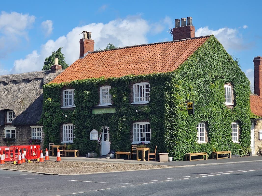 The Wentworth Arms hotel, covered in ivy, features a red-tiled roof and wooden benches outside on a sunny day.