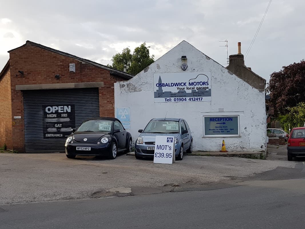 Osbaldwick Motors Ltd garage with two cars parked outside and a sign displaying MOT prices and contact information.