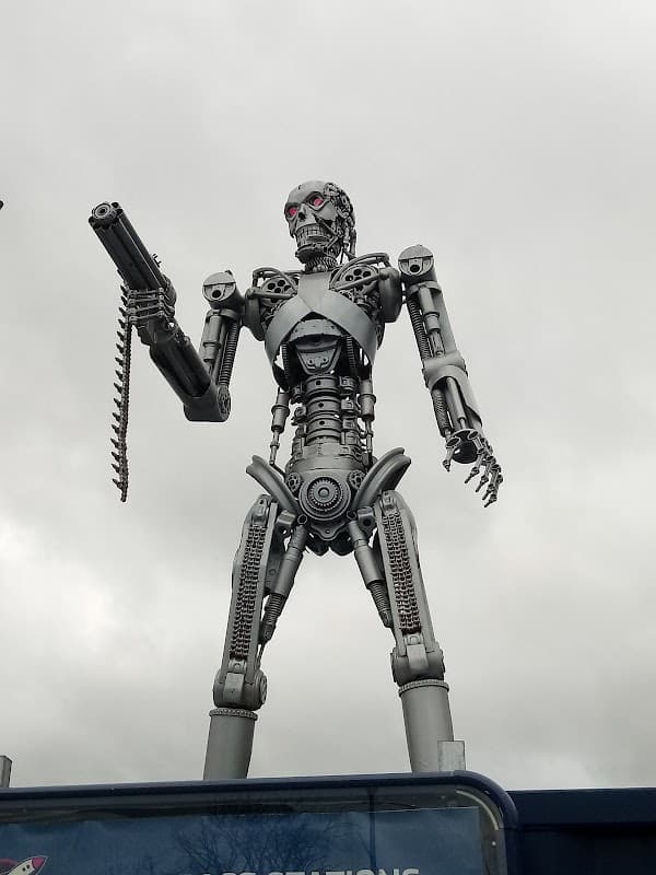 A large metallic robot statue holding a gun, standing on a platform against a cloudy sky.