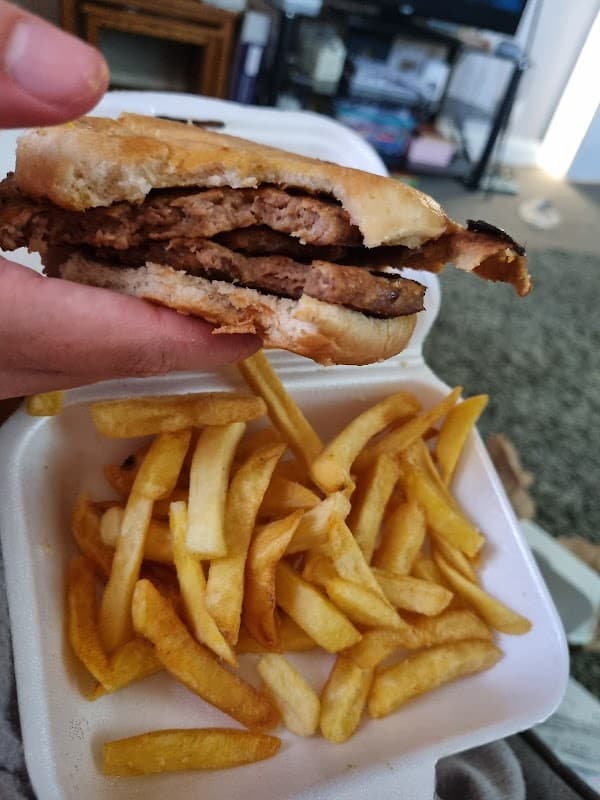 A hand holds a half-eaten burger next to a container of golden fries on a textured surface.