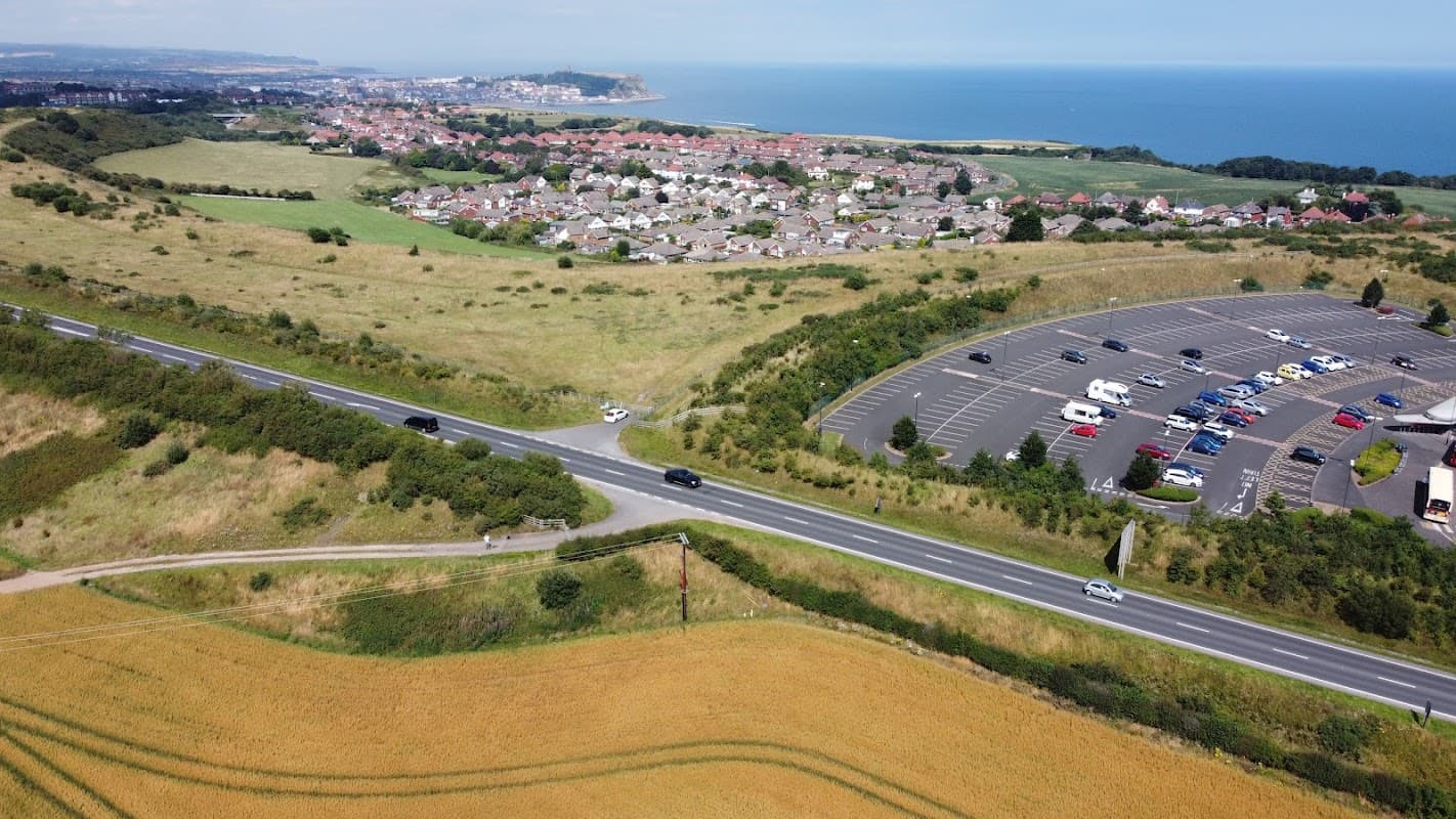 Aerial view of Filey Rd Park & Ride with parked cars, fields, and coastal town in the background.