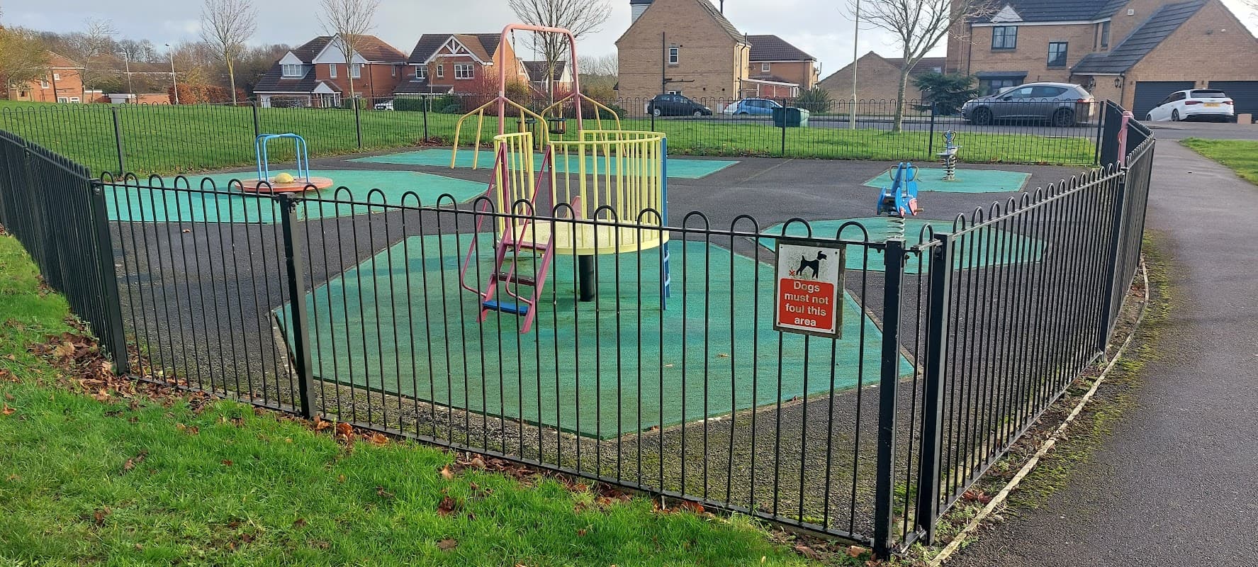 Colorful playground equipment within a fenced area, featuring a spinning structure and slides on green flooring.