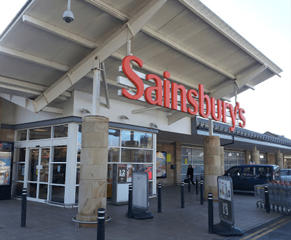 Sainsbury's store entrance with large signage, glass doors, and a modern roof structure in Otley, Yorkshire.