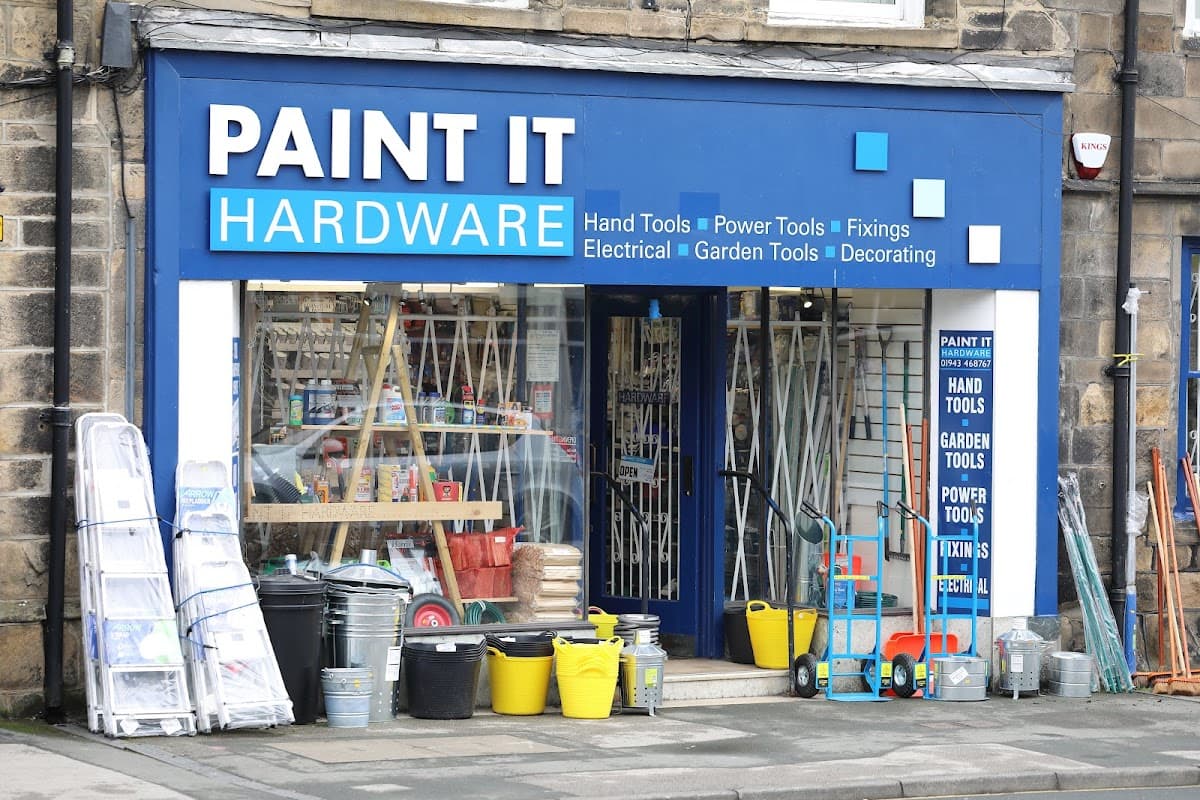 Bright blue storefront with "Paint It Hardware" sign, displaying tools, paint supplies, and garden equipment outside.