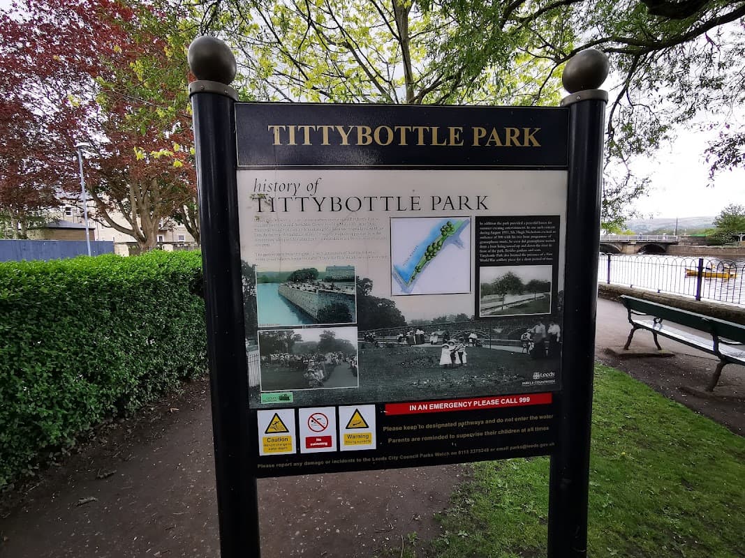 Sign for Tittybottle Park displaying its history, surrounded by greenery and benches in Otley, Yorkshire.