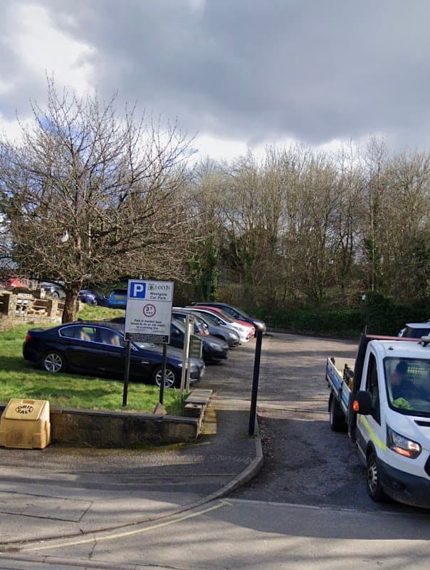 Free parking area with a sign, several parked cars, and a tree under a cloudy sky in Otley, Yorkshire.